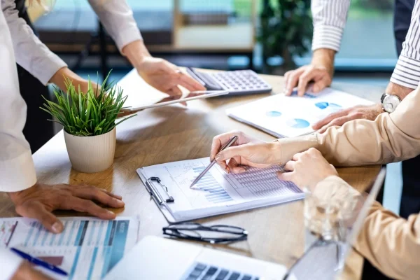 Mehrere Personen analysieren gemeinsam Diagramme und Unterlagen am Tisch und entwickeln Strategien mit umfassendem 360°-Blick für fundierte Entscheidungen.