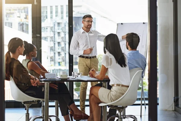 Berater erklärt Strategie am Flipchart vor Team im Meetingraum und vermittelt ganzheitlichen Überblick im Workshop mit 360°-Blick auf Prozesse.