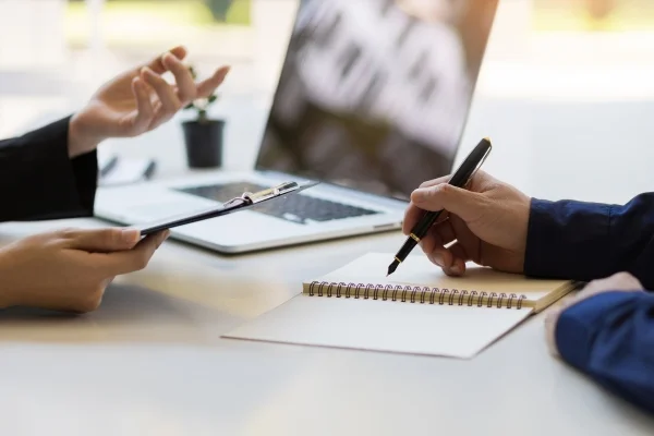 Zwei Personen besprechen Unterlagen am Schreibtisch, machen Notizen und planen Entscheidungen gemeinsam mit strukturiertem 360°-Blick auf Geschäftsprozesse.