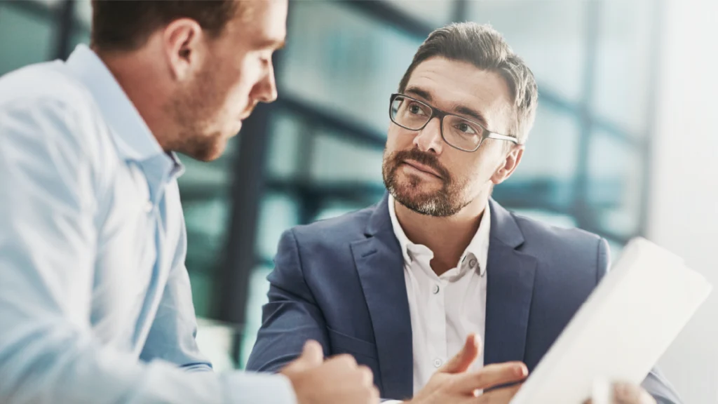 Zwei Fachkräfte im Gespräch mit Unterlagen während eines Führungskräftecoaching, zur Entwicklung von Führungskompetenzen und strategischer Entscheidungsfindung im Unternehmen.