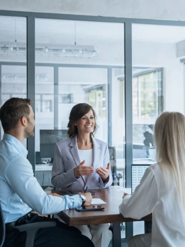 Beraterin spricht mit zwei Kunden am Tisch im modernen Büro und entwickelt gemeinsam individuelle Strategien und passgenaue Individuallösungen.