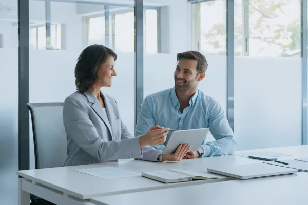 Beraterin erklärt Tablet-Inhalte einem Kunden im Büro und entwickelt gemeinsam mit ihm maßgeschneiderte Strategien und passende Individuallösungen.