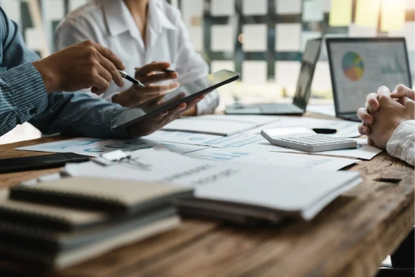 Team analysiert Diagramme und Daten auf Tablet und Unterlagen am Tisch und entwickelt gemeinsam durchdachte Individuallösungen für Geschäftsentscheidungen.