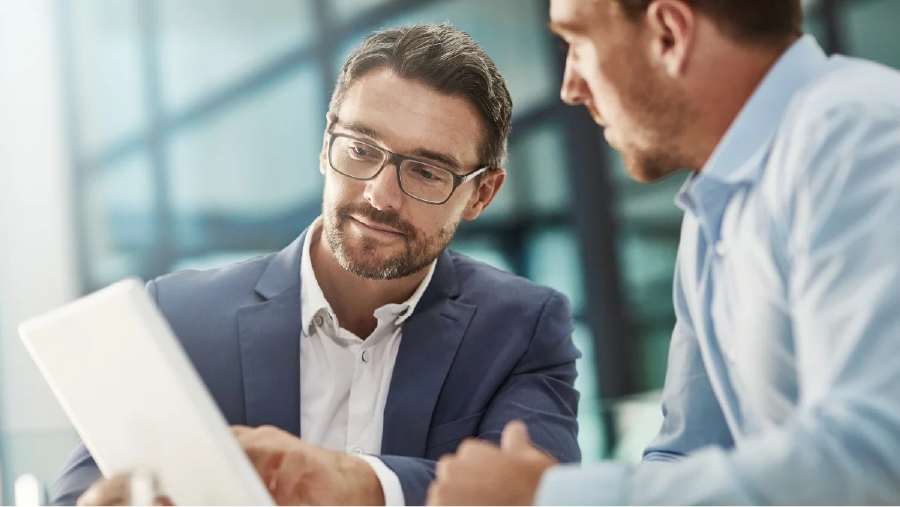 Berater erklärt einem Kunden auf einem Tablet Prozesse und Kennzahlen zur Optimierung von Abläufen im Qualitätsmanagement eines Unternehmens.